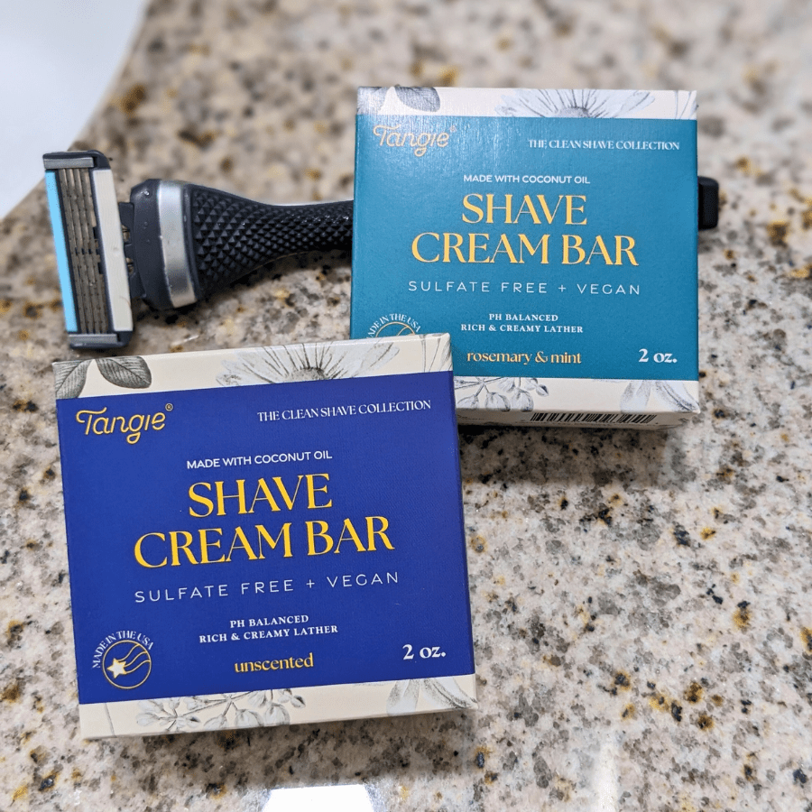 Tangie Shave Cream Bars in Unscented and Rosemary Mint variations, displayed with a razor on a bathroom countertop. A zero-waste, plastic-free shaving alternative.