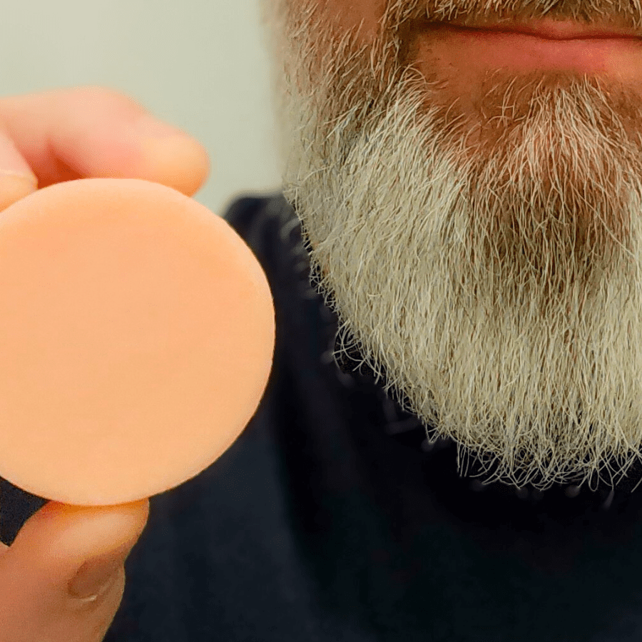 Tangie Beard Conditioning Bar held in hand in front of a bearded face, highlighting the product’s size and solid, plastic-free design.