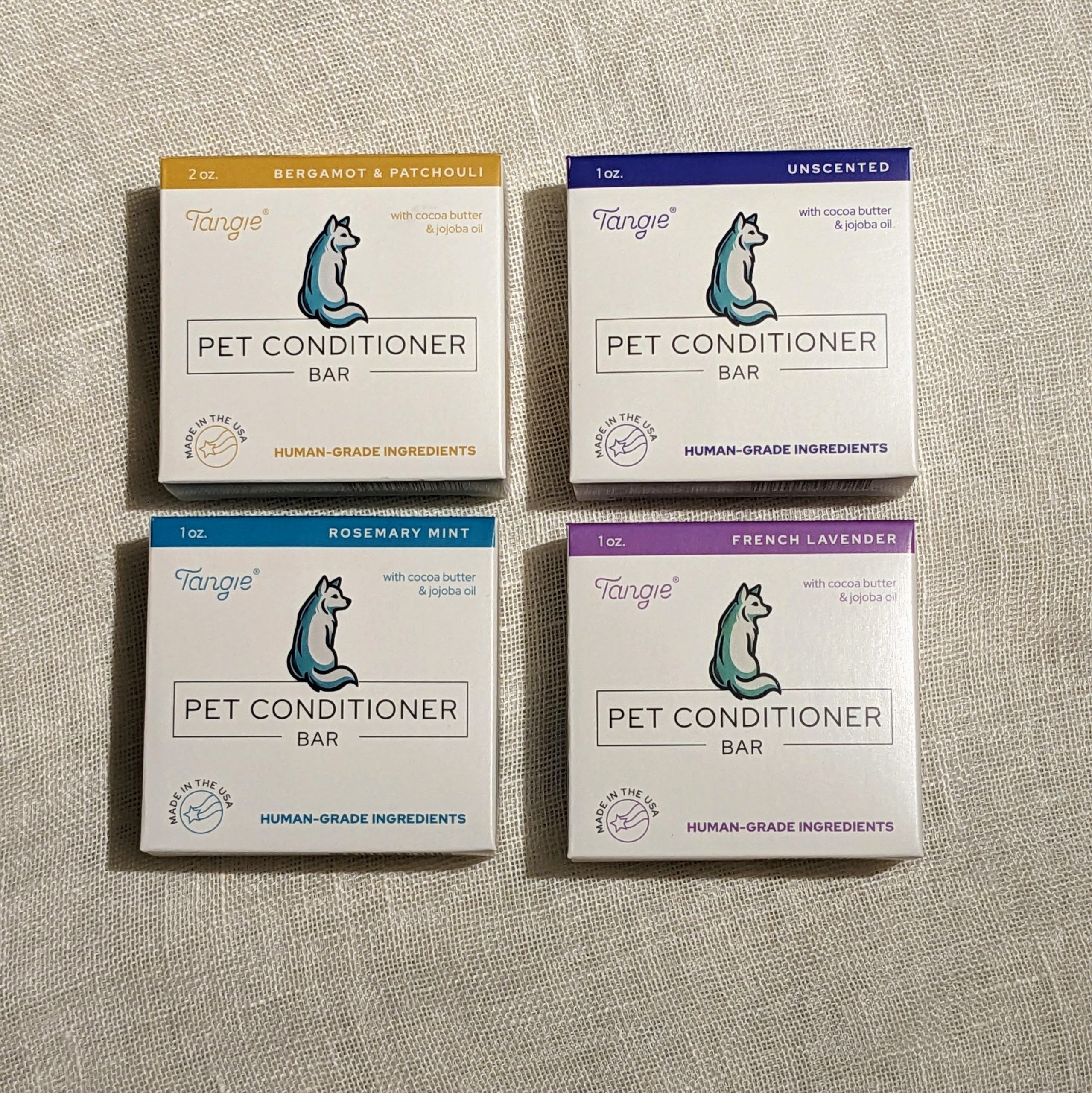 Tangie Pet Conditioner Bars in four variations: Bergamot & Patchouli, Unscented, Rosemary Mint, and French Lavender, displayed on a neutral fabric backdrop.