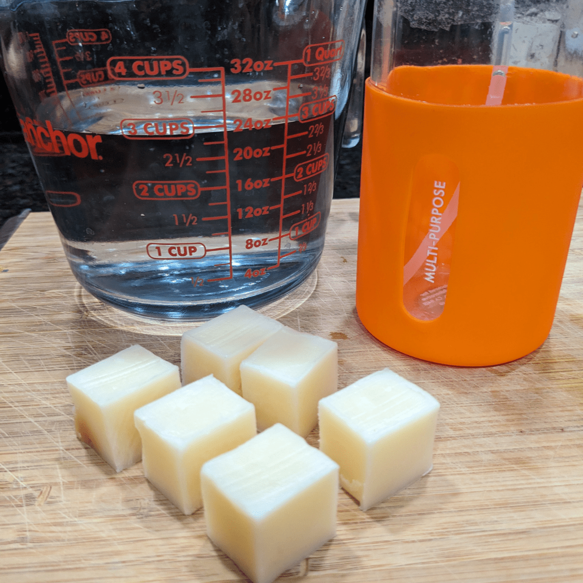 Tangie all-purpose cleaner concentrate pieces with a measuring cup of water and a reusable orange spray bottle.