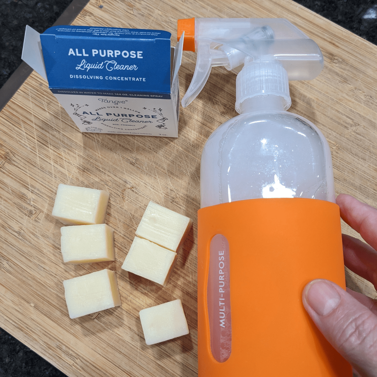 Tangie all-purpose cleaner concentrate with reusable orange spray bottle and bar pieces on a cutting board.