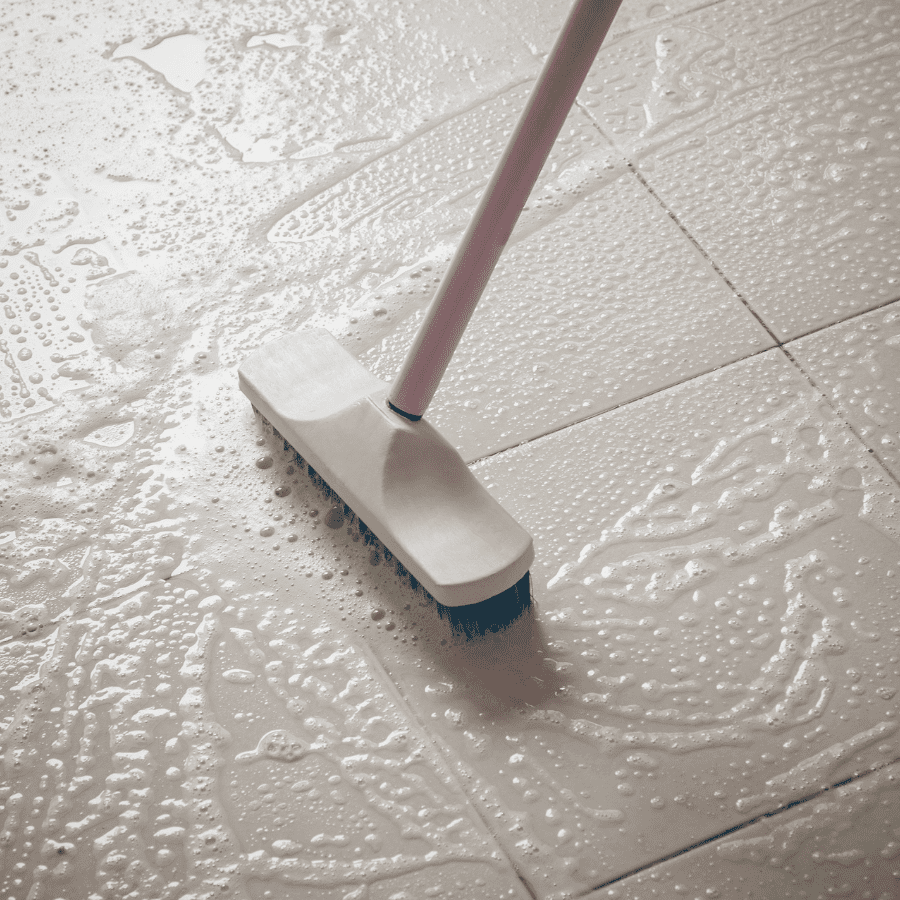 Scrub brush cleaning wet tile floor with dissolved Tangie Floor Cleaner Concentrate